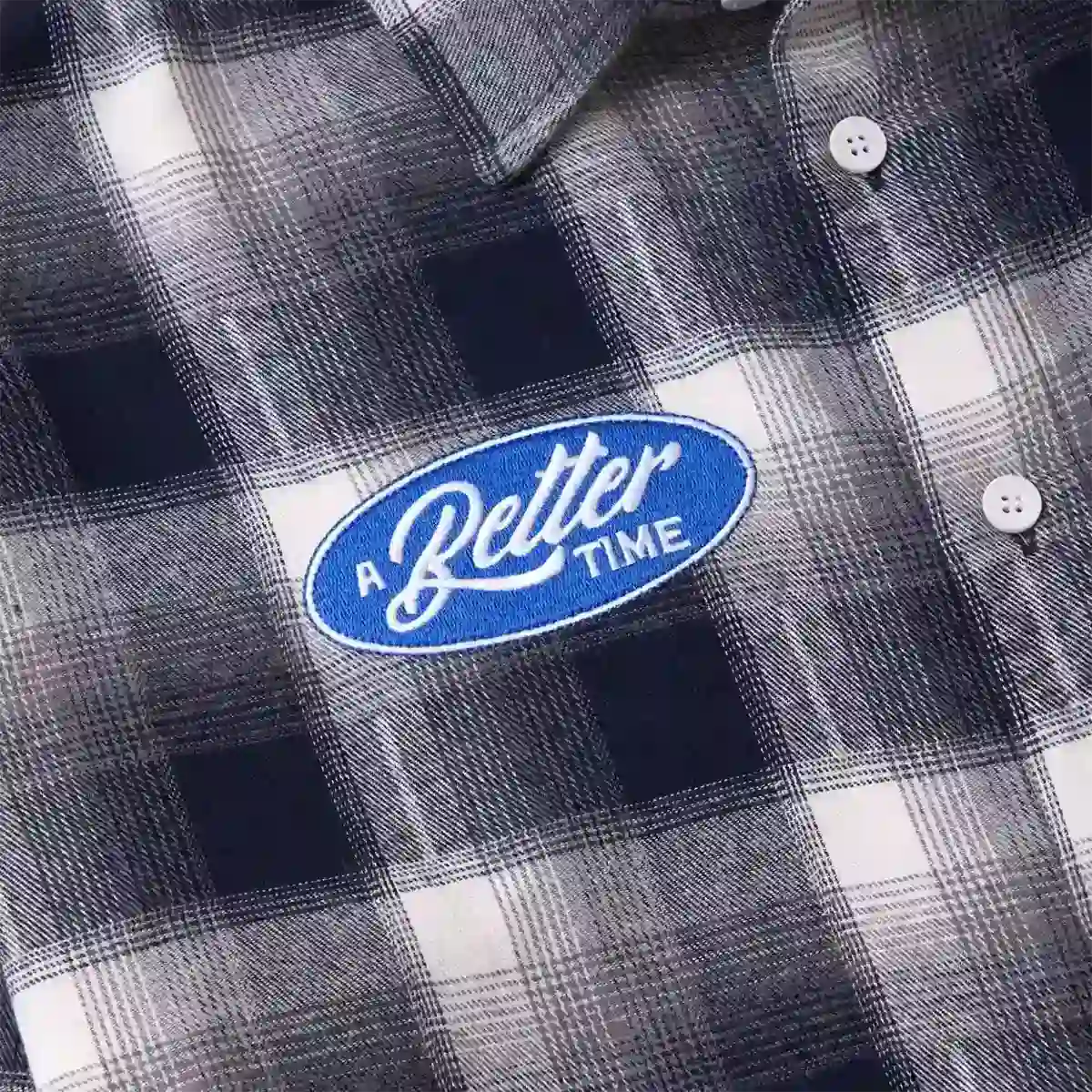Close-up of black plaid flannel shirt with blue oval A Better Time embroidered patch and white buttons