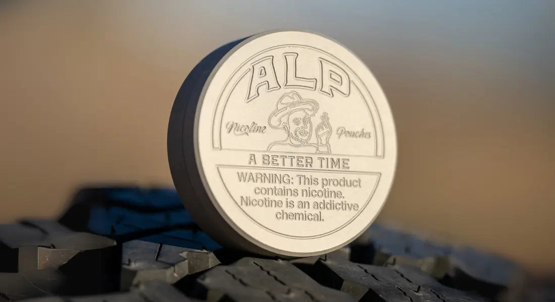 Flavored oral nicotine container with embossed ALP branding placed on a rugged tire surface outdoors.