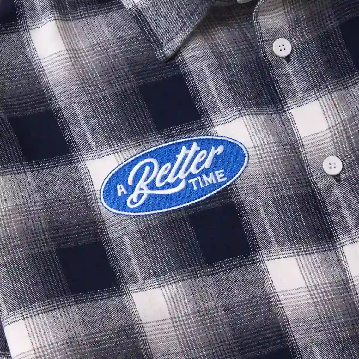 Close-up of black plaid flannel shirt with blue oval A Better Time embroidered patch and white buttons